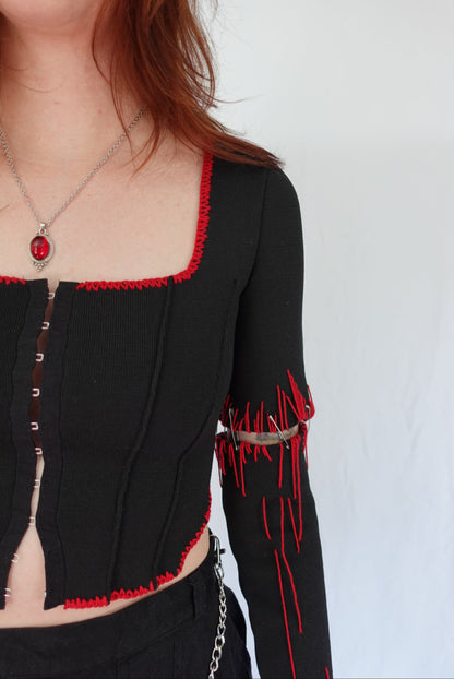 Close-up of a person wearing a black outfit with red accents on a white background
